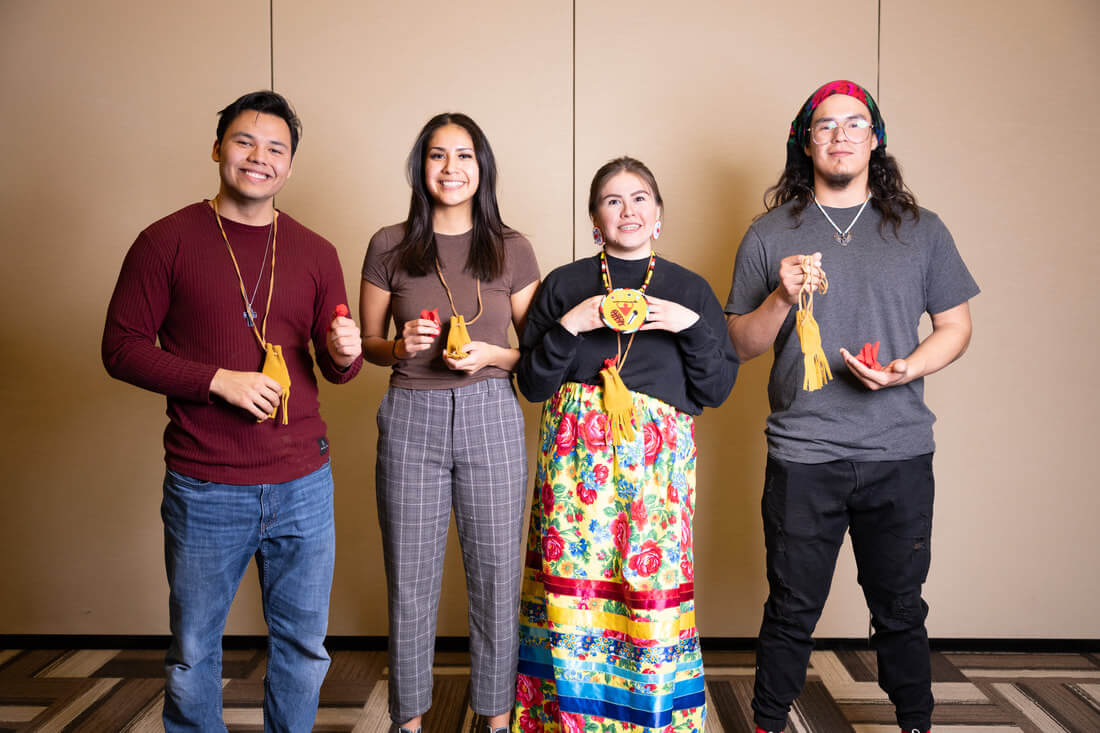 Tobacco Warriors Dillon Campiou, Raquel Healy, Vanessa Kyme-Gilbert and Ethan Yellow Old Woman holding small red pouches of sacred tobacco while standing in conference center hall.