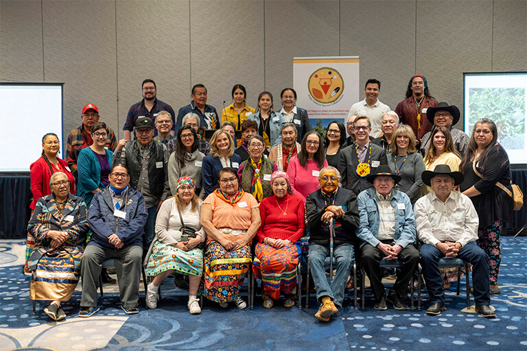 Attendees of Keep Tobacco Sacred conference seated in conference room. Three rows of people with Elders in front and Tobacco warriors in back.