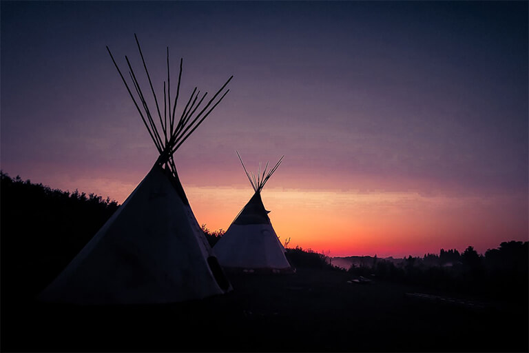 Silhouette of traditional Tipis in front of colorful sunset